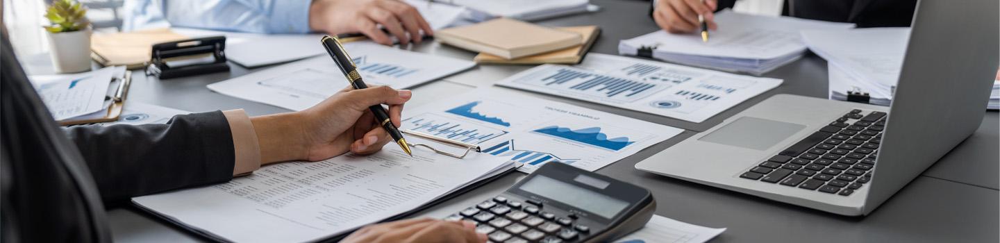 Auditor and accountant review business documents on office table.